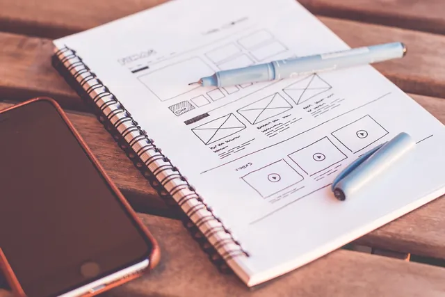Website wireframe sketched in a notebook next to a phone