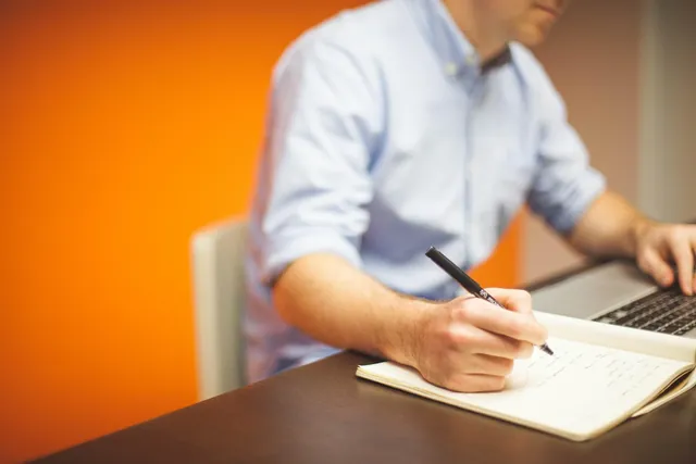 Professional writing a plan in a notebook next to a laptop